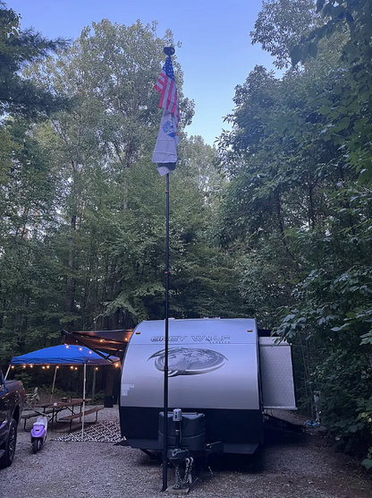Small trailer parked in a wooded area with an American flag on a pole.
